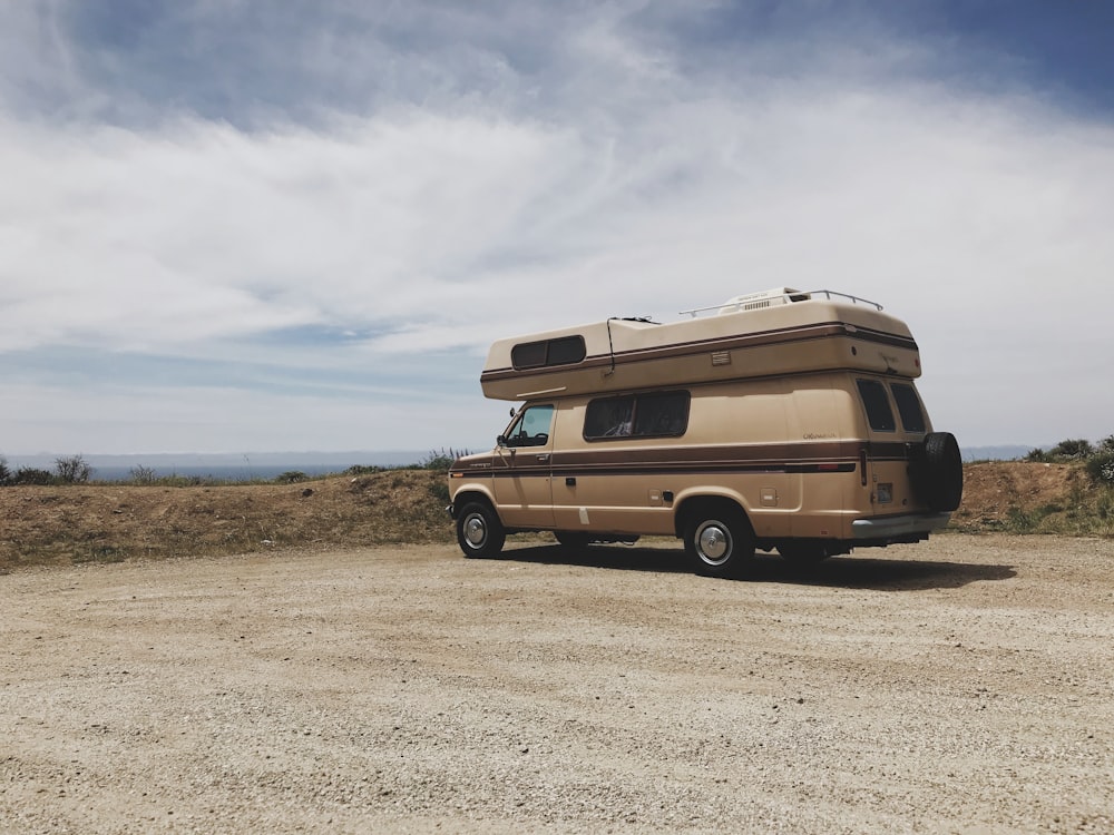 Remorque de camping-car marron et blanc sur un terrain brun sous des nuages blancs et un ciel bleu pendant la journée