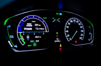 A digital car dashboard displaying various indicators and metrics including speed, power, remaining kilometers, fuel consumption in liters per 100 kilometers, and temperature. The dashboard is illuminated with neon-like blue and green lights, showing additional symbols and alerts related to driving mode and car status.