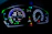 A digital car dashboard displaying various indicators and metrics including speed, power, remaining kilometers, fuel consumption in liters per 100 kilometers, and temperature. The dashboard is illuminated with neon-like blue and green lights, showing additional symbols and alerts related to driving mode and car status.