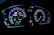 A digital car dashboard displaying various indicators and metrics including speed, power, remaining kilometers, fuel consumption in liters per 100 kilometers, and temperature. The dashboard is illuminated with neon-like blue and green lights, showing additional symbols and alerts related to driving mode and car status.
