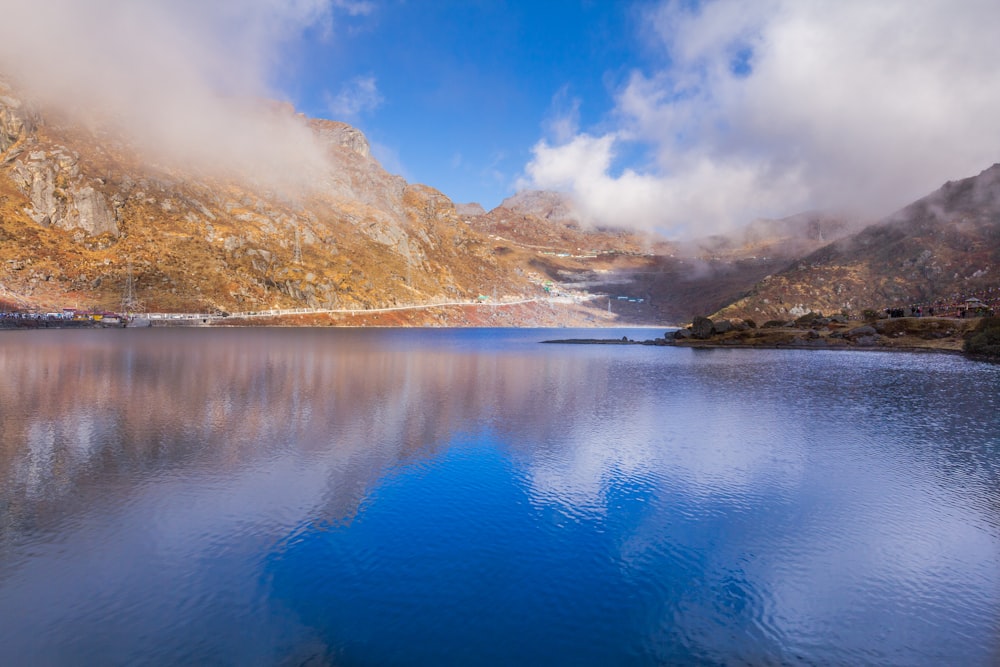 brown and green mountains beside blue lake under blue sky during daytime