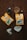 Two packets of Oak & Bond Coffee Co. coffee are placed on a wooden surface with scattered coffee beans. There is a small glass of amber liquid, possibly whiskey or liqueur, next to a dark bottle. A metallic coffee filter holder and a paper filter are also present.