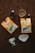 Two packets of Oak & Bond Coffee Co. coffee are placed on a wooden surface with scattered coffee beans. There is a small glass of amber liquid, possibly whiskey or liqueur, next to a dark bottle. A metallic coffee filter holder and a paper filter are also present.