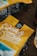 A close-up of a yellow coffee bag with the logo 'Oak & Bond Coffee'. The focus is on the branding, with coffee beans scattered around on a wooden table, creating a rustic and inviting atmosphere.