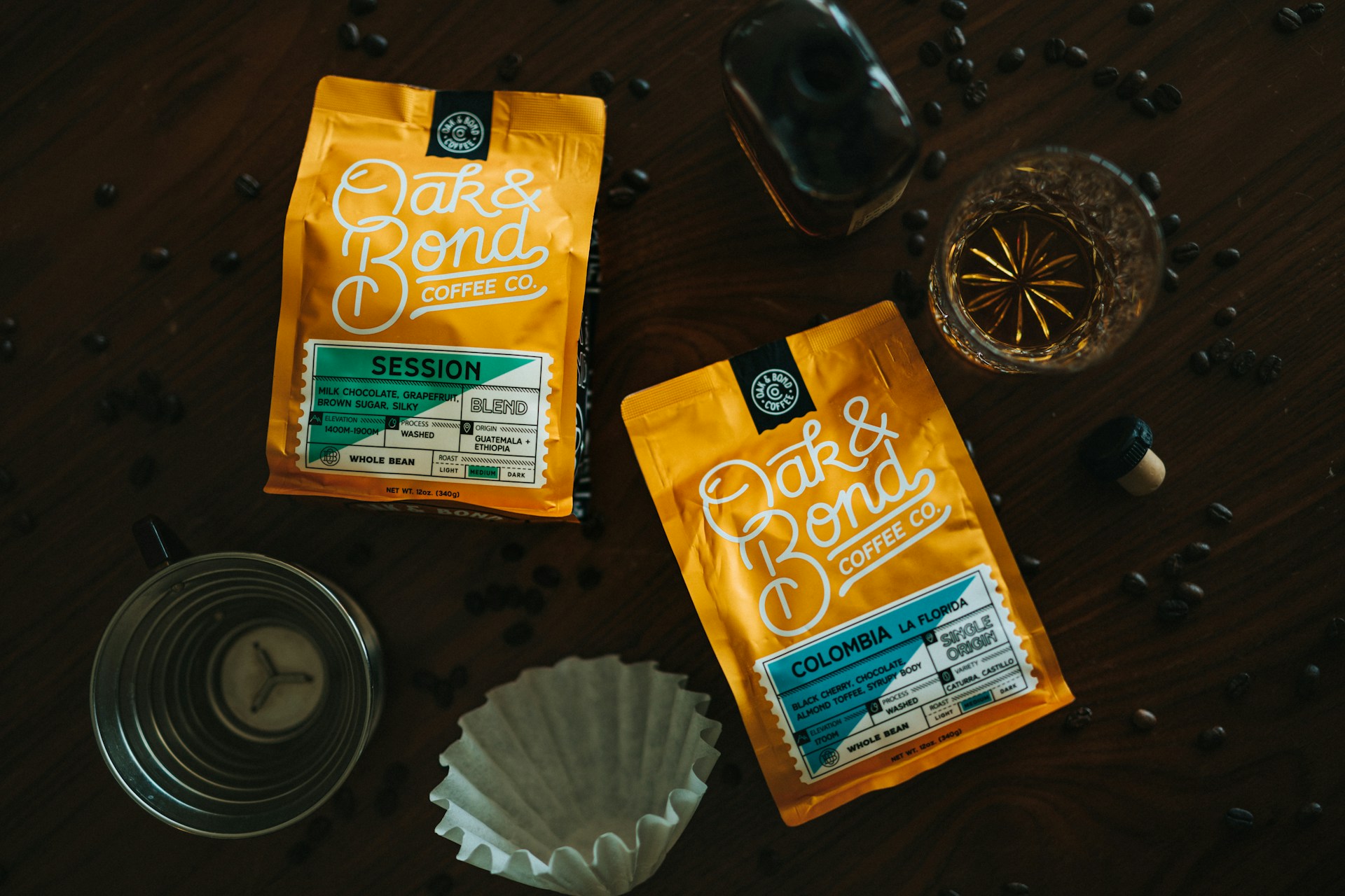 A lively community gathering around a table, sharing coffee brewing tips and laughing, with bags of Bodhi Beans coffee and branded mugs in the foreground.