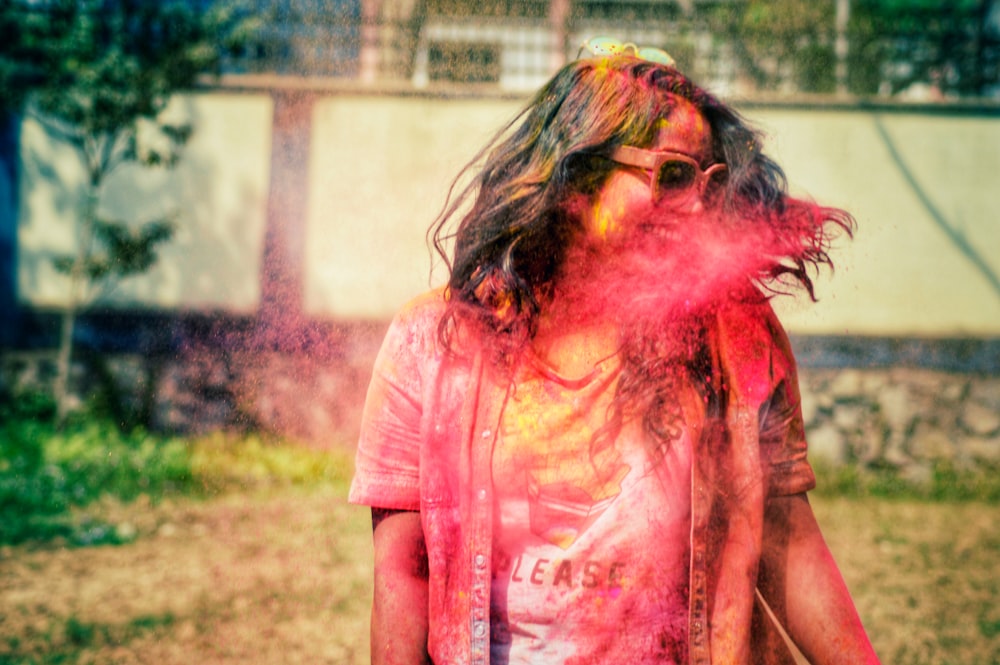 Femme en chemise rose avec de la poudre rouge, jaune et verte sur son visage