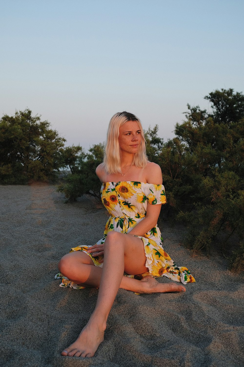 woman in yellow and white floral dress sitting on gray concrete floor