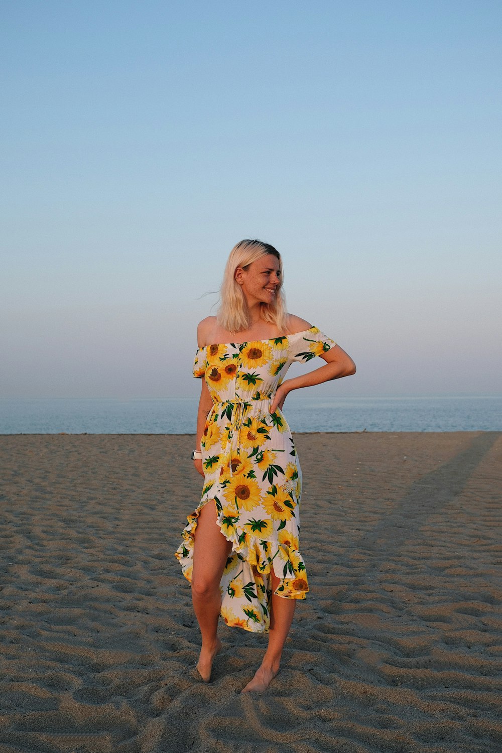 낮 동안 해변에 서 있는 흰색과 노란색 꽃 드레스를 입은 여자