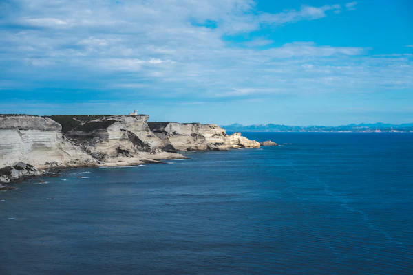 white and black rock formation on blue sea under blue and white cloudy sky during daytime