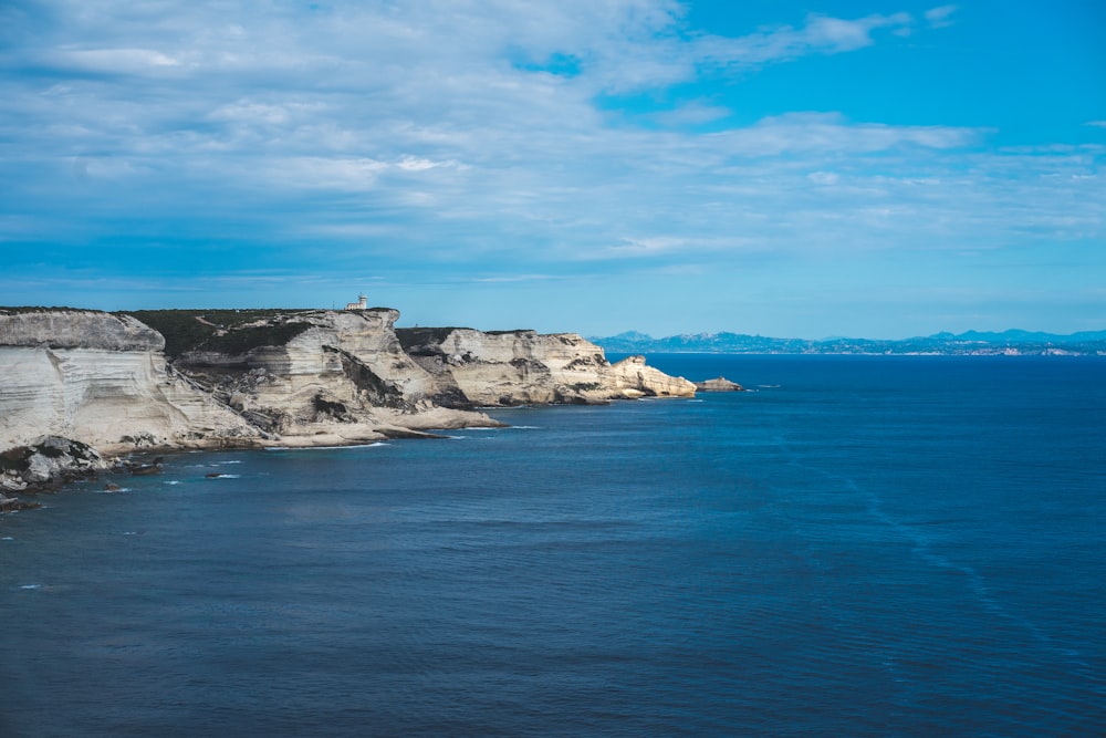 white and black rock formation on blue sea under blue and white cloudy sky during daytime