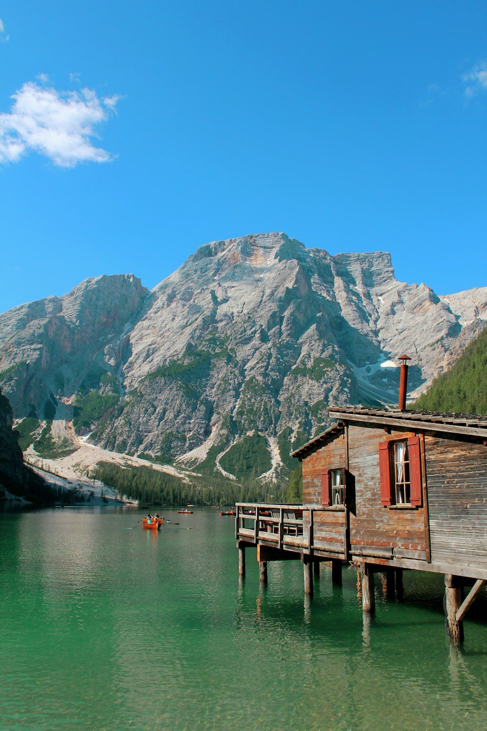 casa de madeira marrom na doca do lago perto da montanha sob o céu azul durante o dia
