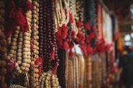A collection of colorful beaded necklaces with tassels is displayed, with beads of various sizes and colors such as beige, brown, and deep red. The necklaces are hanging closely together, creating a dense and vibrant texture.