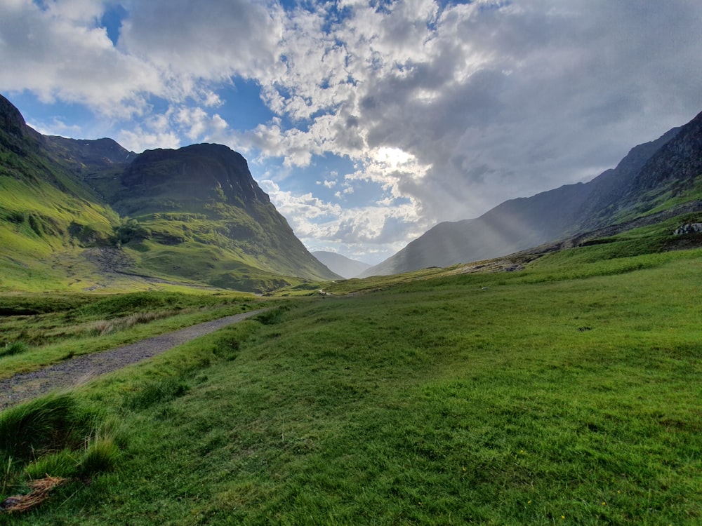 green grass field and mountains under blue sky and white clouds during daytime