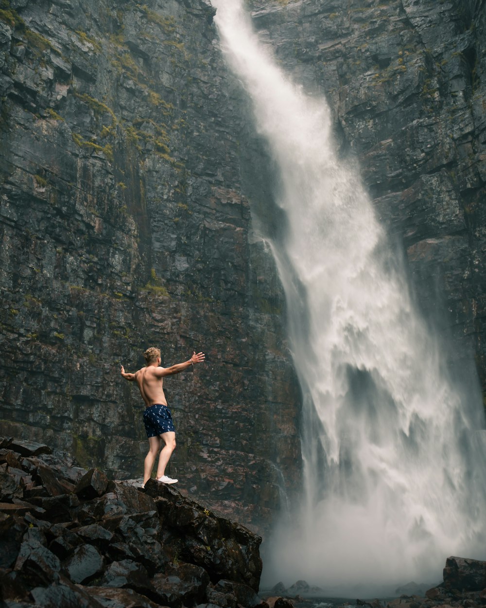 man in black shorts standing on rock formation near waterfalls during daytime