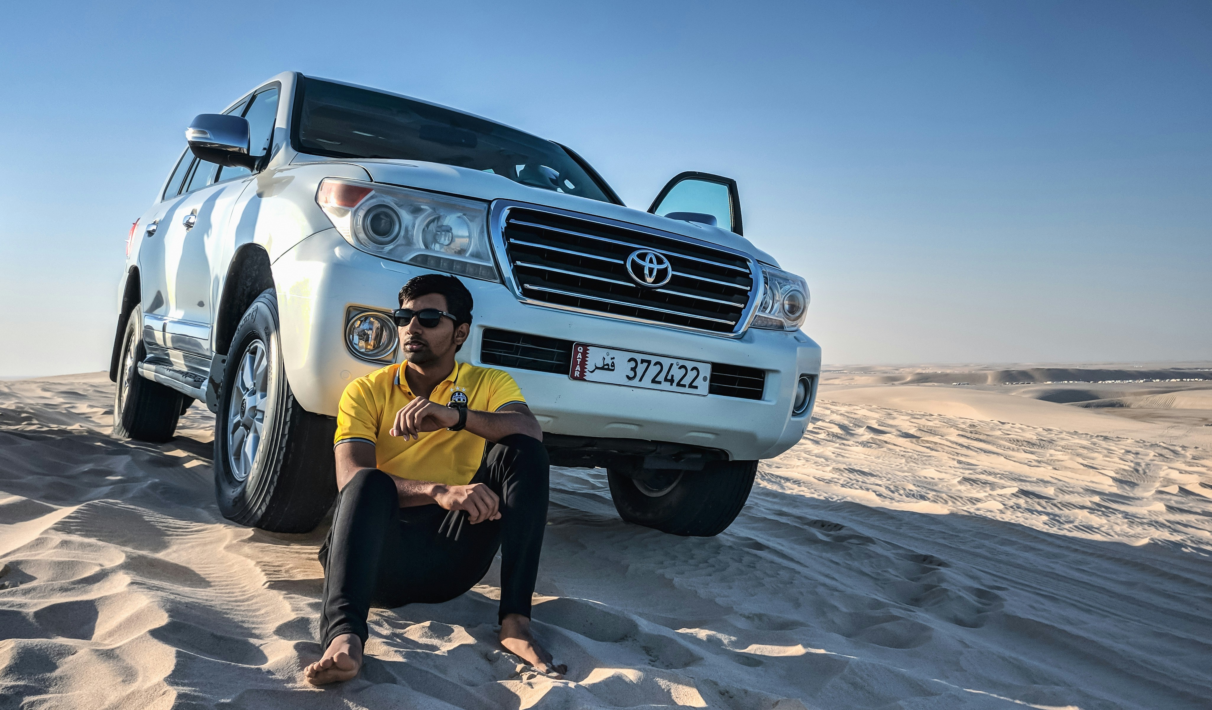 woman in yellow shirt and black pants sitting on white mercedes benz car qatar teams background