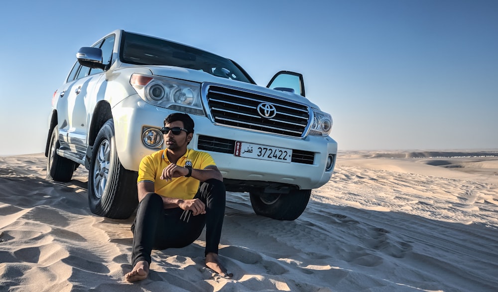 woman in yellow shirt and black pants sitting on white mercedes benz car