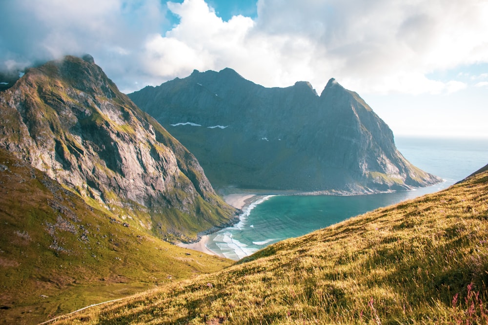 green and brown mountains beside body of water under white clouds during daytime