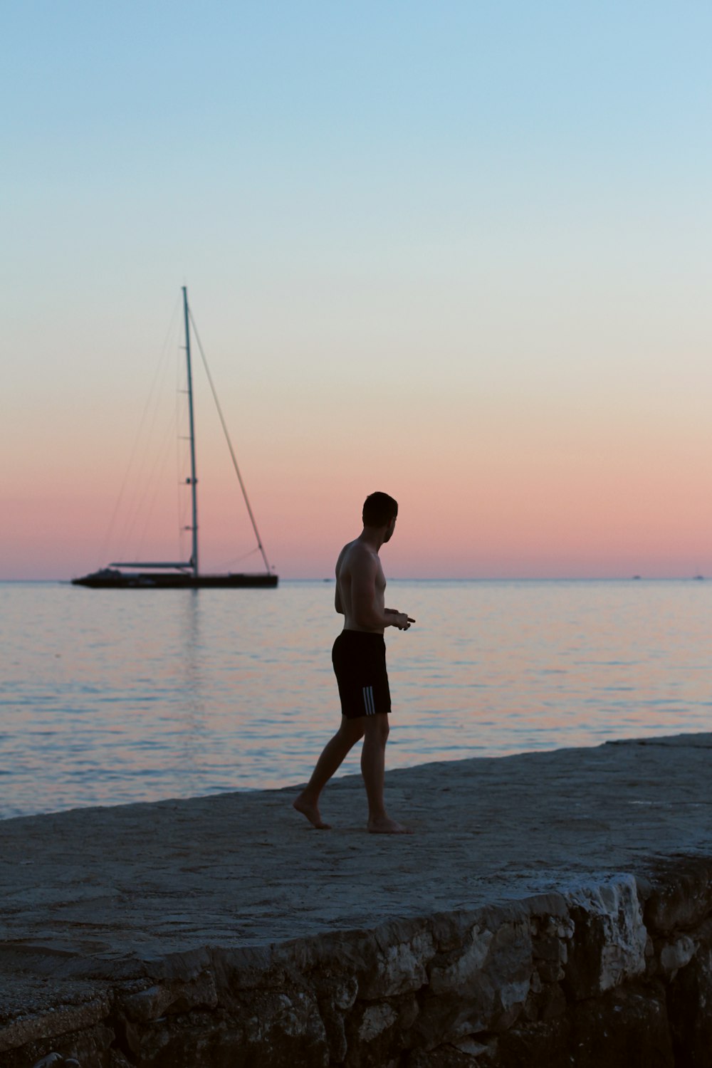 Hombre en pantalones cortos negros de pie en la playa durante la puesta del sol