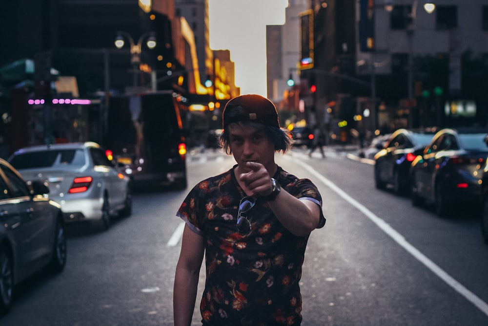 man in black and white floral shirt standing on sidewalk during night time