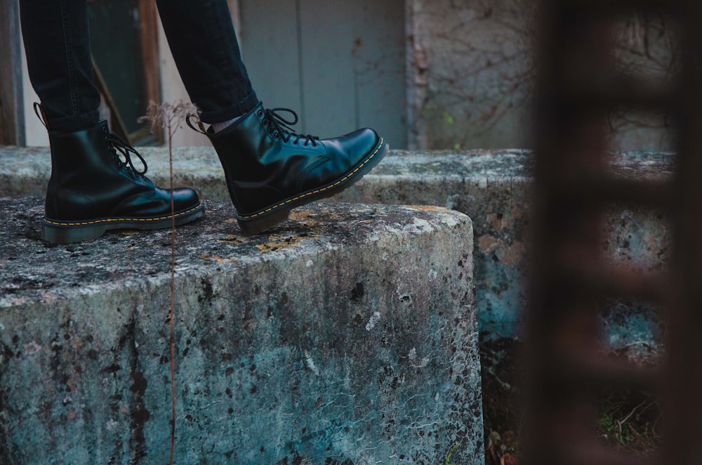 person in black leather shoes standing on gray concrete wall