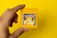 A hand holding a yellow Game Boy cartridge with a vibrant Pokémon label featuring Pikachu on a solid yellow background.