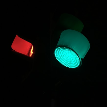 A traffic light with a prominent green light illuminated above a red light, set against a dark background. The green light is bright and LED-lit, providing a stark contrast to the surrounding darkness.