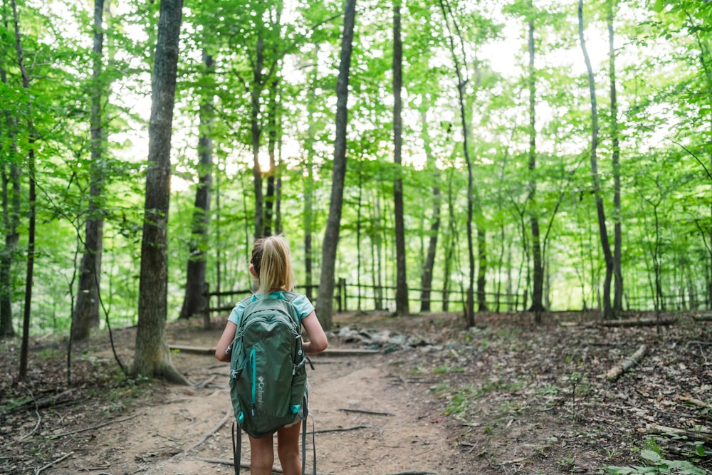 Frau im grünen Rucksack geht tagsüber durch den Wald