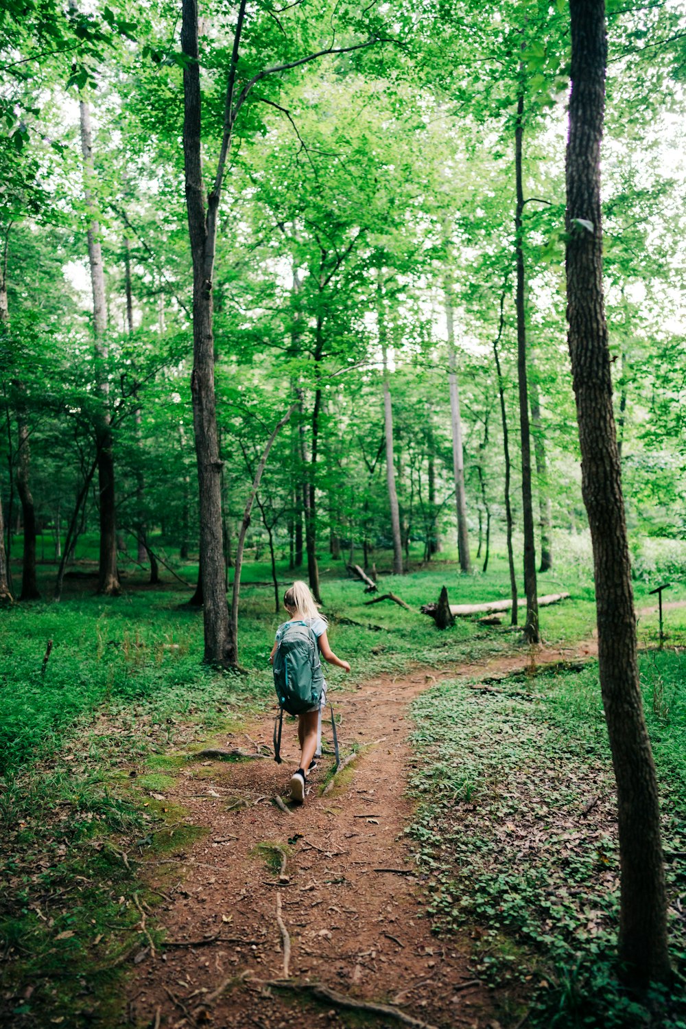 Mujer con chaqueta de mezclilla azul caminando en el bosque durante el día
