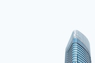 A modern high-rise office building with a sleek glass exterior. The architectural design features curved lines and a minimalist aesthetic. The building stands prominently against a pale, light gray sky, emphasizing its height and contemporary style.