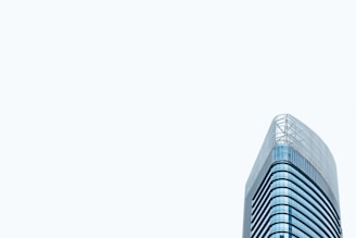 A modern high-rise office building with a sleek glass exterior. The architectural design features curved lines and a minimalist aesthetic. The building stands prominently against a pale, light gray sky, emphasizing its height and contemporary style.