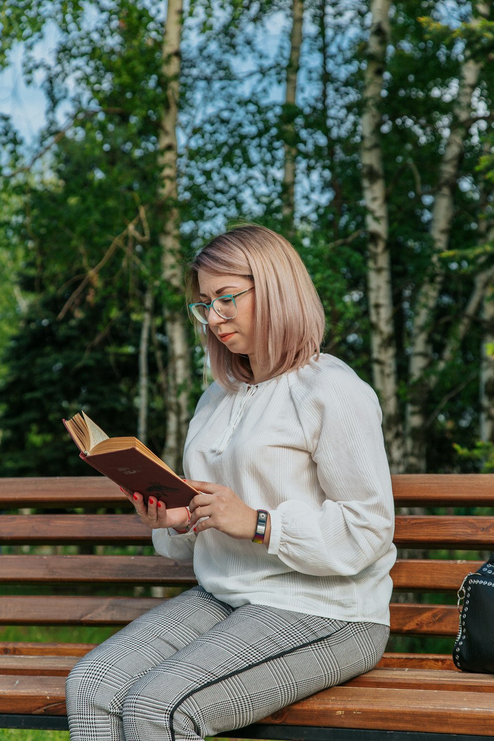 woman in white sweater sitting on brown wooden bench reading book