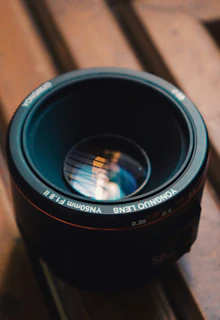 A sleek camera lens resting on a dark surface with golden light reflecting softly, evoking creativity and focus.