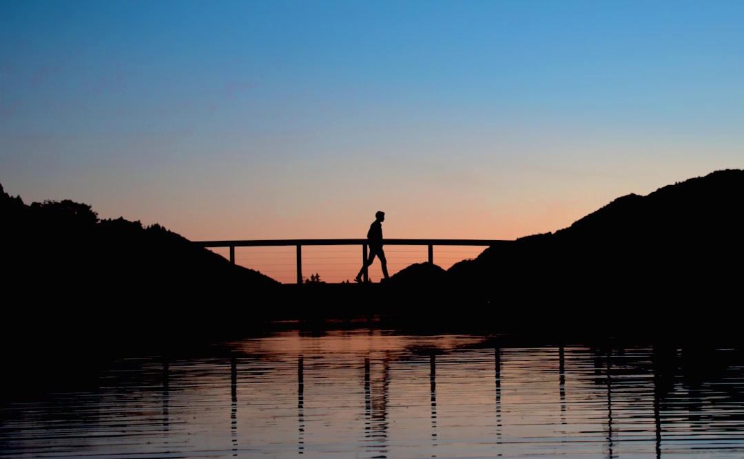 silhouette of man standing on dock during sunset, Silhouette of a person walking over a bridge on a lake during sunset