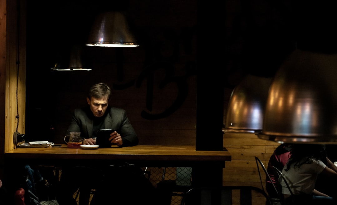 man in black suit jacket sitting beside brown wooden table