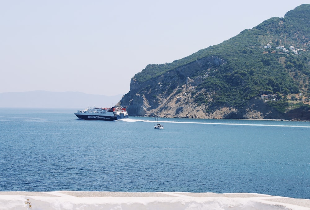 white and black boat on sea near green mountain during daytime