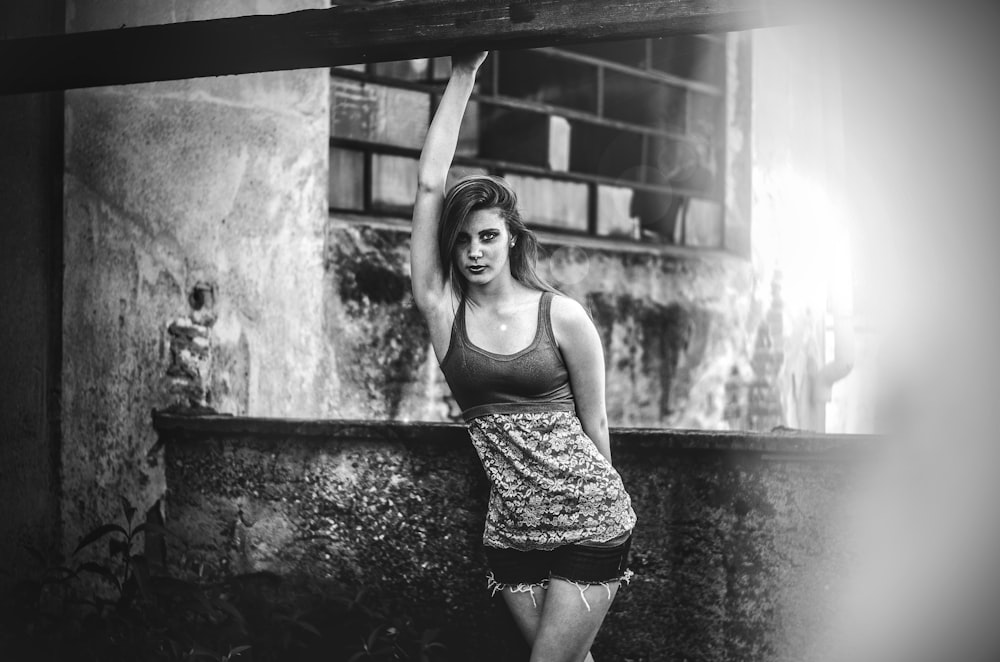 grayscale photo of woman in tank top and shorts standing near wooden post