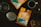 Two bright orange bags of Oak & Bond Coffee Co. are displayed on a wooden table. A cup of coffee, a metal coffee dripper, a paper filter, and a bottle with a cork are arranged around them, along with scattered coffee beans.