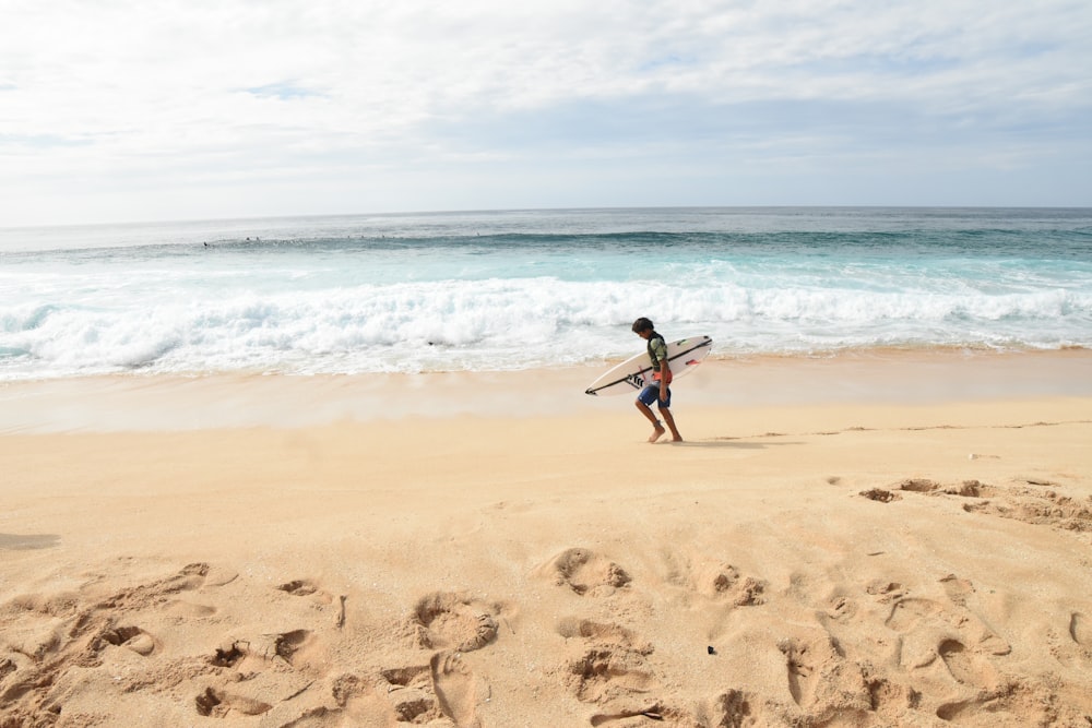 man in black shorts carrying white surfboard walking on beach during daytime