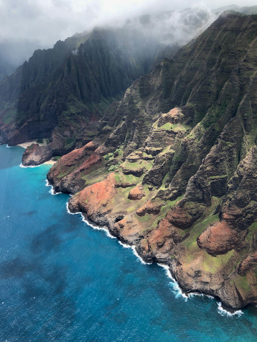 brown and green mountain beside blue sea during daytime