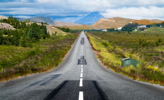 gray asphalt road between green grass field during daytime in Varmaland Iceland