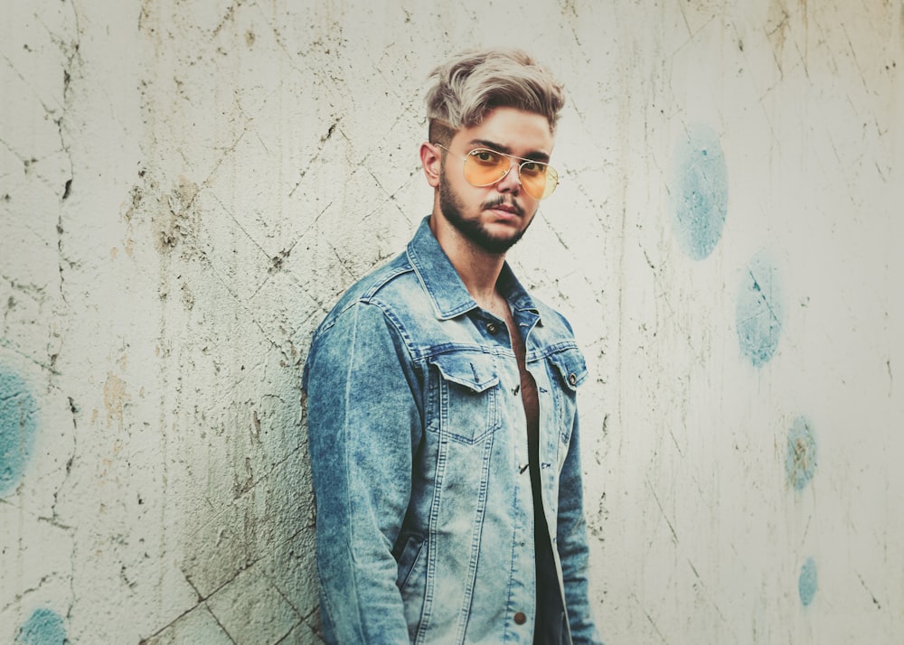 man in blue denim jacket leaning on white wall