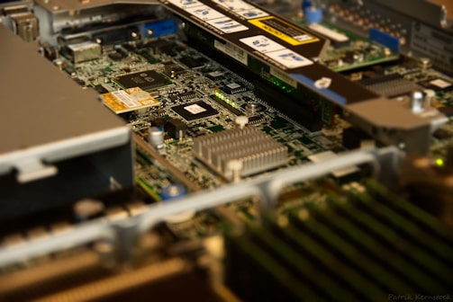 A close-up view of a computer motherboard with various components such as chips, heat sinks, and circuit traces. The image captures the intricate details and layout of the hardware, emphasizing the metallic and green colors typical of electronic components.