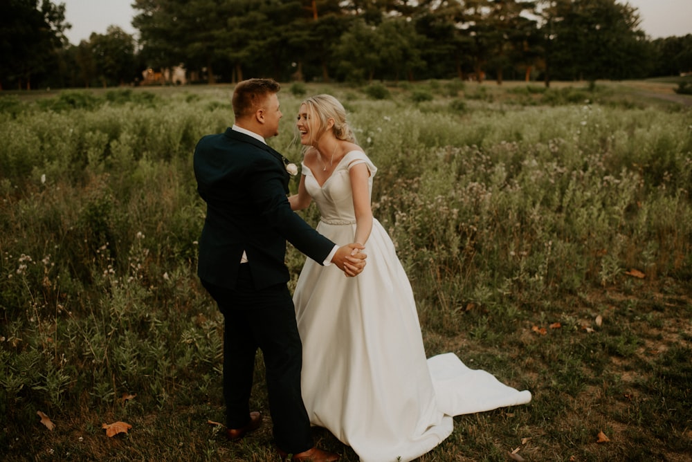 man in black suit kissing woman in white wedding dress on green grass field during daytime