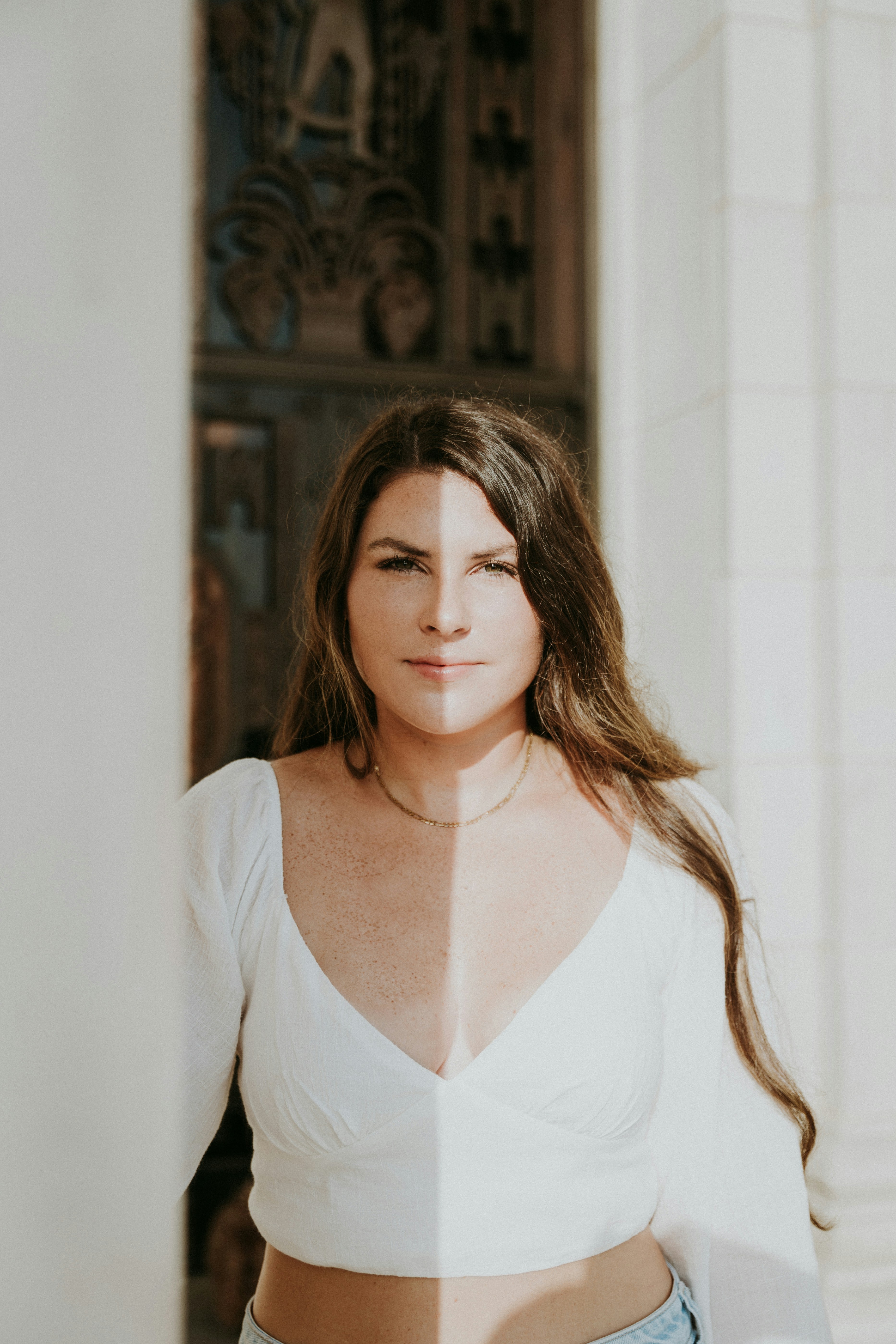 Donna con maglia bianca in piedi davanti a muri di pietra scolpita.