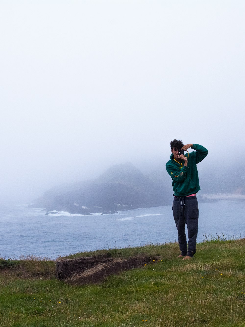 man in green hoodie standing on green grass field near body of water during daytime