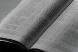 An open book with printed text on its pages, showing a focus on the paragraphs and detailed written content. The lighting is soft, creating a calm and studious atmosphere.