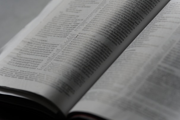 An open book with printed text on its pages, showing a focus on the paragraphs and detailed written content. The lighting is soft, creating a calm and studious atmosphere.
