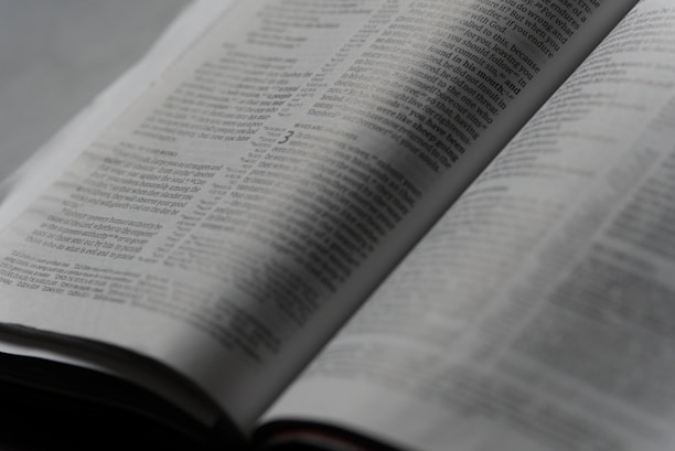 An open book with printed text on its pages, showing a focus on the paragraphs and detailed written content. The lighting is soft, creating a calm and studious atmosphere.