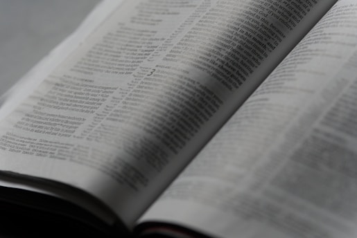 An open book with printed text on its pages, showing a focus on the paragraphs and detailed written content. The lighting is soft, creating a calm and studious atmosphere.