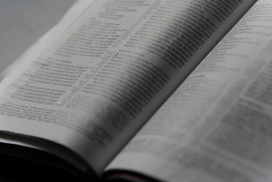 An open book with printed text on its pages, showing a focus on the paragraphs and detailed written content. The lighting is soft, creating a calm and studious atmosphere.